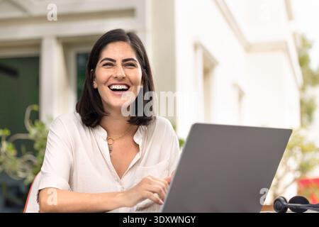 Joyeuse jeune femme hispanique travailleuse à distance assise sur le lieu de travail Banque D'Images