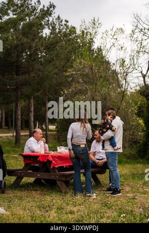 Les membres de la famille se réunissent autour d'une table de pique-nique, dégustant un repas détendu en plein air Banque D'Images