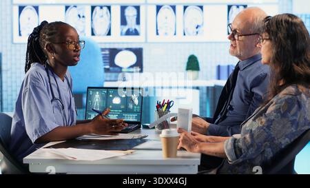 Personnel médical afro-américain expliquant les résultats des tests à un couple âgé, examinant les résultats du diagnostic en cabinet médical. Utilise une technologie médicale avancée pour évaluer les examens IRM. Caméra B. Banque D'Images