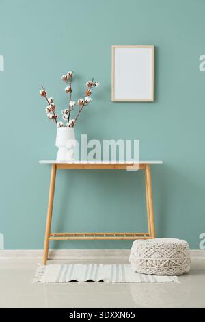 Pouf, table et vase avec des fleurs de coton près du mur vert à l'intérieur du salon Banque D'Images