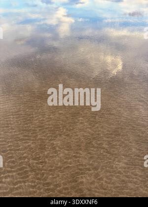 Reflets de nuages et de ciel sur le sable doré ondulant dans les eaux peu profondes de la plage Banque D'Images