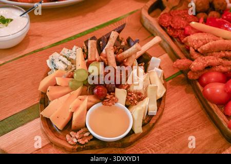 un plateau de fromage avec différents types de fromage, raisins, noix, gressins et un petit bol de miel. Banque D'Images
