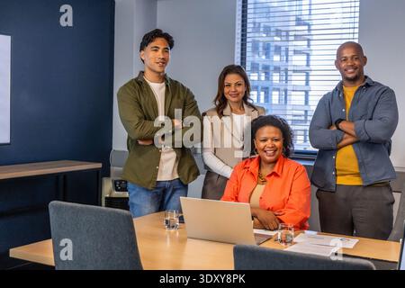 Divers collègues se réunissent à la table de conférence dans une tenue d'affaires décontractée avec ordinateur portable et papiers Banque D'Images
