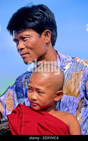 Un homme et son fils sont assis ensemble. Le père a l'air attentionné pendant que le garçon regarde devant lui. Ils sont au Myanmar sous un ciel dégagé. Banque D'Images