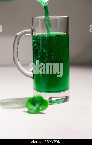 Verser de la bière verte mousseuse dans une tasse en verre avec du trèfle. – Patricks Day Irish Beer Celebration. photographie Banque D'Images