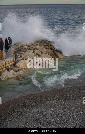 Les gens se tiennent près d'une jetée de défense maritime alors qu'une grande vague méditerranéenne s'écrase, Nice, France. Mer agitée, temps orageux. Banque D'Images