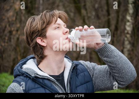 Athlète et sportif homme caucasien buvant de l'eau de la bouteille dans le parc public après l'entraînement. À l'extérieur. Bilan hydrique. Formation jeune homme en extérieur Banque D'Images