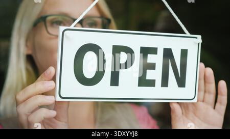 La vendeuse tourne la tablette qui dit fermé à ouvert. Début de journée, ouvrez votre concept d'entreprise Banque D'Images