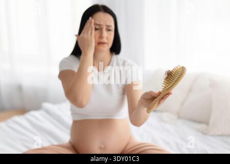 Femme enceinte inquiète en regardant la perte de cheveux sur la brosse à la maison Banque D'Images
