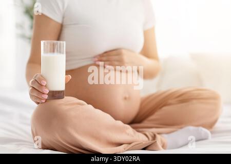 Femme enceinte tenant un verre de lait tout en touchant le ventre assis sur le lit Banque D'Images