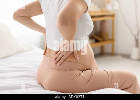 Gros plan d'une femme enceinte touchant le bas du dos alors qu'elle était assise sur le lit Banque D'Images