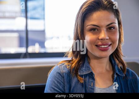 Thirtything femme assise sur le banc près de la fenêtre dans le salon, portant du denim et souriant, espace de copie Banque D'Images
