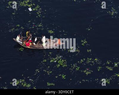 Vue aérienne d'un petit bateau en bois transportant des gens coupe à travers les eaux sombres du Buriganga, au milieu de la végétation éparpillée, Dhaka, Dhaka Division, Banque D'Images