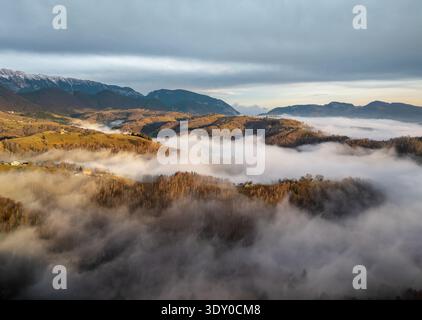 Vue aérienne du paysage avec la vallée enveloppée dans une épaisse couverture de brouillard, avec les montagnes au loin, Șirnea, Brașov, Roumanie. Banque D'Images