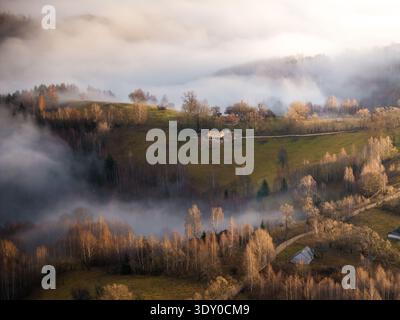 Vue aérienne d'un paysage où la brume se tisse à travers les vallées, couvrant la terre dans une étreinte douce et éthérée, Șirnea, Brașov, Roumanie. Banque D'Images
