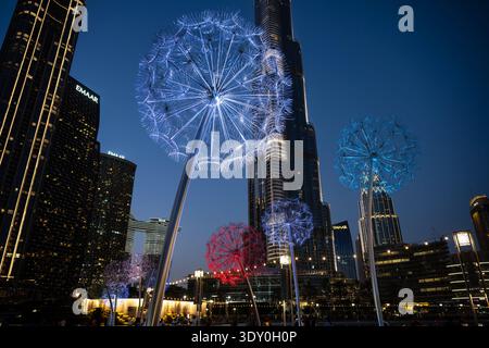Un cliché de nuit sous-jacent avec de grandes installations artistiques illuminées en forme de pissenlit au premier plan. Les sculptures brillent de lumières bleues et rouges Banque D'Images