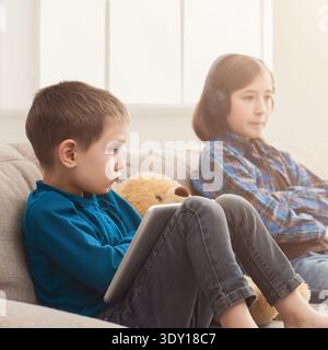 Deux enfants avec des gadgets sur le canapé à la maison Banque D'Images