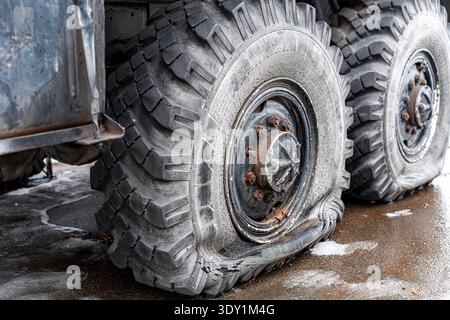 Vue d'un pneu crevé sur un camion lourd, assis sans vergogne sur l'asphalte humide, sa bande de roulement robuste dégonflée contre le sol impitoyable, Kiev, Ukraine Banque D'Images