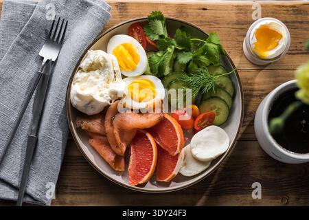 Plaque de petit déjeuner saine à haute teneur en protéines avec œufs durs, saumon fumé, concombres frais, tomates cerises, herbes, tranches d'agrumes et café noir sur Banque D'Images