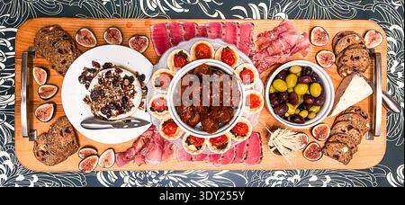 Assiette de charcuterie gourmande avec prosciutto, tranches de thon, olives, figues, fromage et petites bouchées disposées sur une planche de bois. Banque D'Images