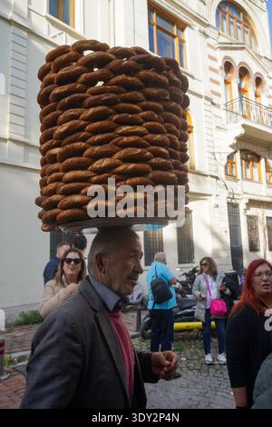 Un vendeur local équilibre habilement une énorme pile de pain simit sur sa tête. Scène culinaire de rue authentique dans un quartier historique avec des touristes. Banque D'Images