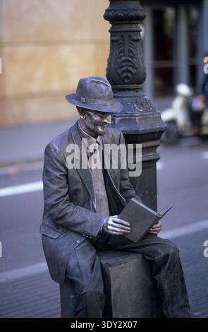 Une statue vivante artiste de rue habillée comme un homme de bronze lisant un livre sur la Rambla, Barcelone, Espagne. Banque D'Images