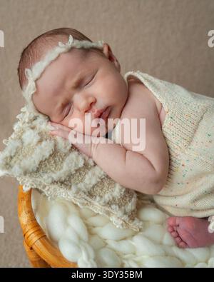 Portrait en gros plan d'une petite fille nouveau-née endormie reposant paisiblement sur un tissu tricoté doux. Tons neutres chauds et détails délicats Banque D'Images