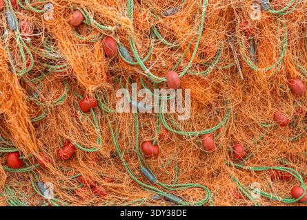 Gros plan détaillé du filet de pêche orange traditionnel avec des cordes vertes. Fond nautique vibrant pour l'industrie maritime et les concepts de fruits de mer. Banque D'Images