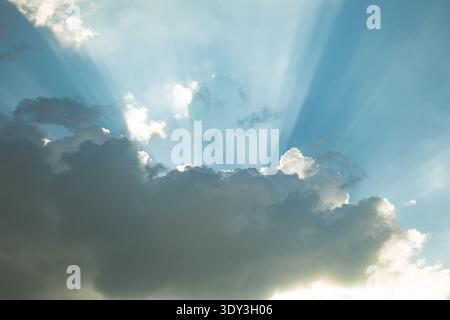 Rayons de soleil perçant à travers les nuages de cumulus sombres créant des rayons lumineux brillants dans le ciel bleu Banque D'Images