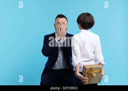 Garçon surprenant son père avec un cadeau sur fond bleu clair Banque D'Images