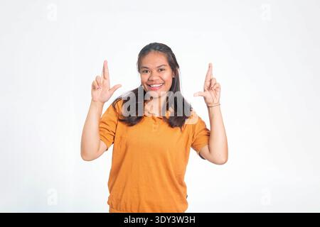 Heureuse femme indonésienne en chemise orange croisant les doigts sur les deux mains, regardant la caméra avec un sourire plein d'espoir et joyeux. Banque D'Images