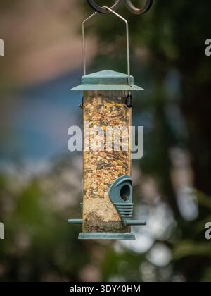 Gros plan d'une mangeoire à oiseaux suspendue de jardin remplie de graines mélangées, invitant les oiseaux dans un cadre de jardin naturel Banque D'Images