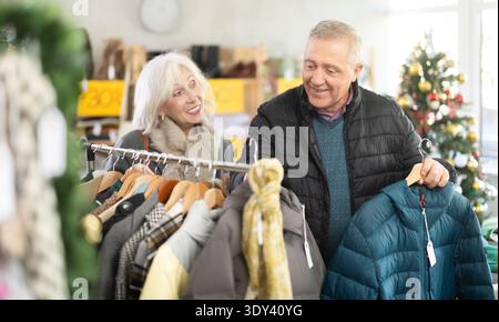 Couple âgé debout dans le magasin de Noël et choisissant des vestes Banque D'Images