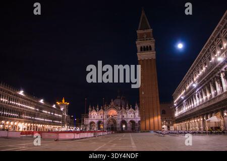 La basilique Saint-Marc illuminée la nuit par la tour géante Campanile s'élevant à droite sous une lune brillante à Venise, en Italie. Banque D'Images