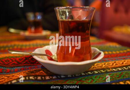 Un verre fumant de thé turc traditionnel servi dans un verre en forme de tulipe sur une nappe tissée authentique et colorée. Banque D'Images