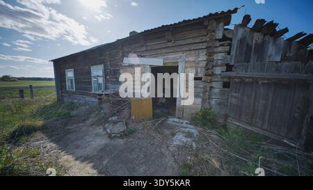 Maison rurale abandonnée en bois montrant la pourriture et la négligence dans un vaste paysage verdoyant Banque D'Images