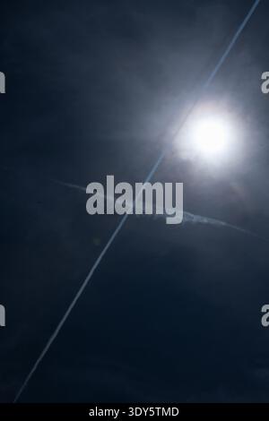 Ciel sombre avec un soleil éclatant et deux traînées d'avion qui se croisent créant une croix Banque D'Images