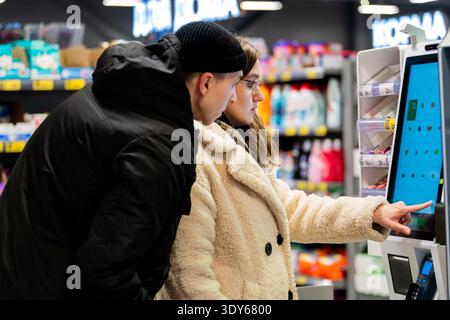 Jeune couple scannant l'épicerie à la caisse libre-service dans un supermarché Banque D'Images