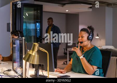 Divers collègues travaillant dans des bureaux ouverts, femme en haut vert parlant dans un casque, espace de copie Banque D'Images