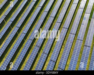Vue aérienne de panneaux solaires photovoltaïques disposés en rangées diagonales à travers des prairies vertes. Ferme d'énergie renouvelable avec disposition systématique du réseau gen Banque D'Images