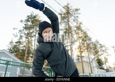 Gros plan d'un homme de quarante ans faisant un virage latéral avec un bras levé à l'extérieur. Il se réchauffe par un matin froid, se concentrant sur la forme. Banque D'Images