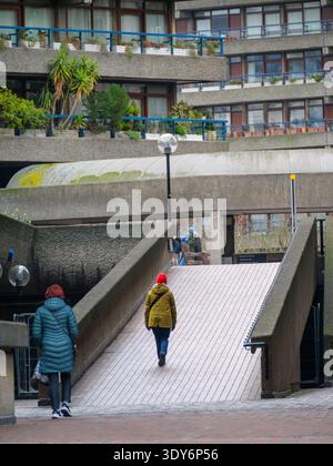 Les piétons montent la rampe de béton de White Lyon court, un carrefour clé dans le système de passerelles de haut niveau (Pedway) du Barbican Estate, Londres. En février 2026, cette artère reste un lien piétonnier essentiel reliant London Wall et Moorgate au Barbican Centre et à l'entrée de Silk Street de la Guildhall School of Music & Drama Banque D'Images
