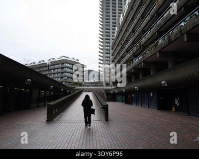 Un piéton monte la rampe de béton de White Lyon court, un carrefour clé dans le système de passerelles de haut niveau (Pedway) du Barbican Estate, Londres. En février 2026, cette artère reste un lien piétonnier essentiel reliant London Wall et Moorgate au Barbican Centre et à l'entrée de Silk Street de la Guildhall School of Music & Drama Banque D'Images