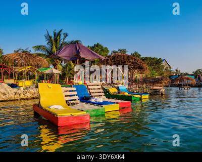 Les visiteurs se détendent sur des chaises longues colorées au Swing Bar au bord de l'eau pendant une journée ensoleillée au Belize Banque D'Images