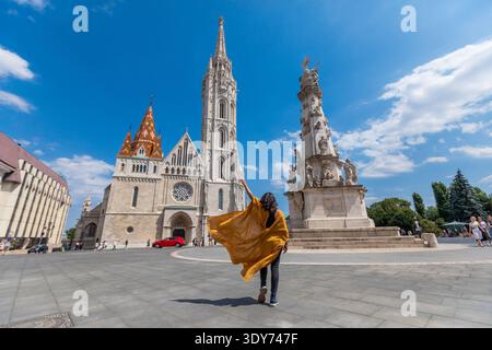 Voyageur en manteau jaune marche vers l'église Matthias et la colonne de la Sainte Trinité à Budapest par une journée ensoleillée Banque D'Images
