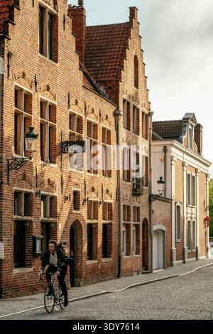 Les cyclistes passent devant des bâtiments historiques dans une rue calme de Bruges pendant la lumière du soir Banque D'Images