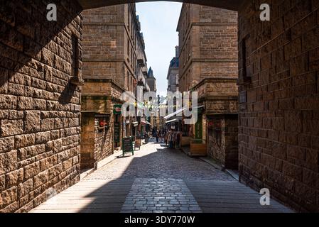 Arc ensoleillé montre rue pavée avec boutiques et décorations dans la vieille ville de Saint-Malo en Bretagne France Banque D'Images