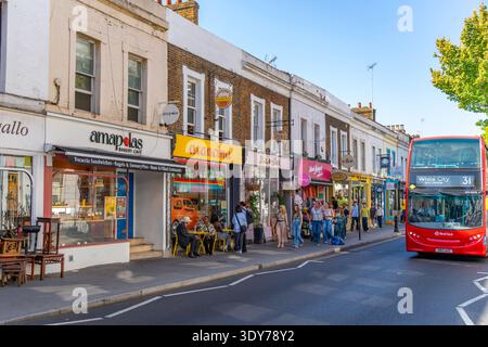 Les gens profitent de l'été à Kensington avec des magasins locaux et un bus qui passe par une journée ensoleillée à Londres, Angleterre, Royaume-Uni Banque D'Images