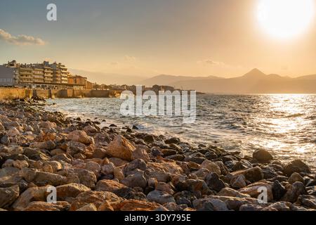 Coucher de soleil sur la côte avec des rochers et des bâtiments à Héraklion, Crète, Grèce Banque D'Images