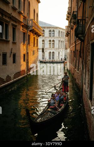 Gondole transporte les touristes à travers les canaux dans le quartier Castello de Venise pendant le coucher du soleil en Vénétie, Italie Banque D'Images
